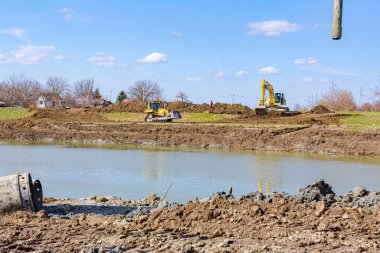 Kazıcılar ve buldozer toprağı dümdüz ediyor, nehir kıyısını eşitliyor, köprü temeli projesi devam ediyor.