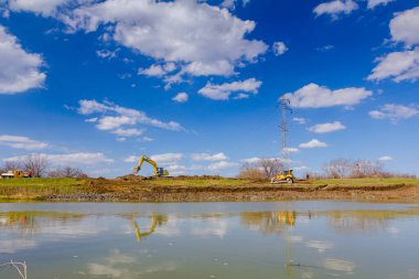 Kazıcılar ve buldozer toprağı dümdüz ediyor, nehir kıyısını eşitliyor, köprü temeli projesi devam ediyor.