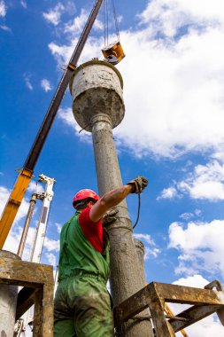 Rigger, güvenlik miğferi ile çalışan işçi, kanalı dikey şarj etmek için pompalar, nehir kıyısındaki köprü temeline taze beton döker..
