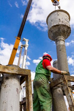 Rigger, güvenlik miğferi ile çalışan işçi, kanalı dikey şarj etmek için pompalar, nehir kıyısındaki köprü temeline taze beton döker..