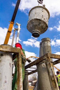 Rigger, güvenlik miğferi ile çalışan işçi, kanalı dikey şarj etmek için pompalar, nehir kıyısındaki köprü temeline taze beton döker..