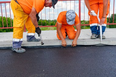 Zrenjanin, Voyvodina, Sırbistan - 8 Haziran 2021: İşçiler köprünün yol kenarını sudan korumak için zift renkli siyah bant takıyorlar. Su yalıtımı malzemesi, suyun kaldırıma yerleştirilen eklem yerinden geçmesini engellemek ve direnmek için tasarlandı.