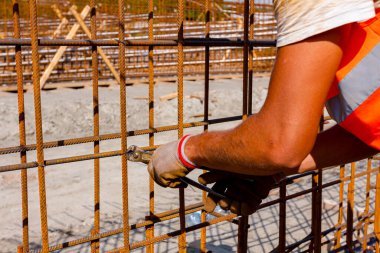 İşçi beton kiriş için takviye bir çerçeve yapmak için pense kullanarak demir çubuğu tel ile bağlıyor. İnşaat alanında çalışıyor.