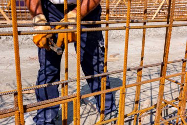 İşçi beton kiriş için takviye bir çerçeve yapmak için pense kullanarak demir çubuğu tel ile bağlıyor. İnşaat alanında çalışıyor.
