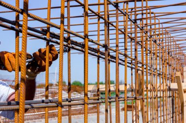 İşçi beton kiriş için takviye bir çerçeve yapmak için pense kullanarak demir çubuğu tel ile bağlıyor. İnşaat alanında çalışıyor.