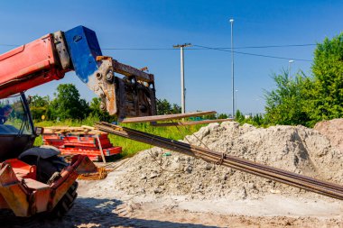 Teslimat ve ulaşım için forklift makineleri, yerden seçilen uzun paslı armatür çubuklarını inşaat alanından kaldırıyor.