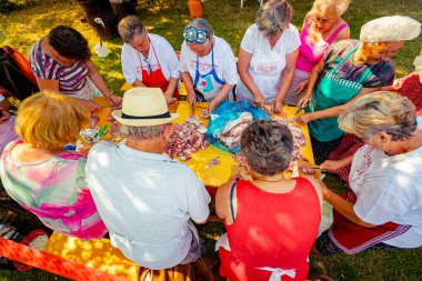 Yaşlılar, yaşlılar, emekliler, erkek ve kadınlar ayakta duruyor ve taze çiğ eti tahta tahtalarda küçük parçalara ayırıyor. Açık havada bıçaklar kullanıyorlar..