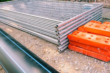 Geçici metal çit panelleri için yığınla galvanizli parça yığıldı ve sokaktaki plastik çit ayaklar inşaat alanının etrafına monte edilmeye hazır..