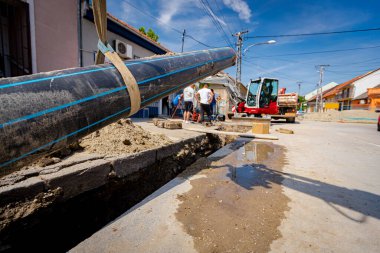 Kauçuk sürüngenli küçük kazıcı siperin yanında duruyor. Kayışlar büyük bir tesisat, plastik HDPE boru hattı yeraltı su şebekesi..