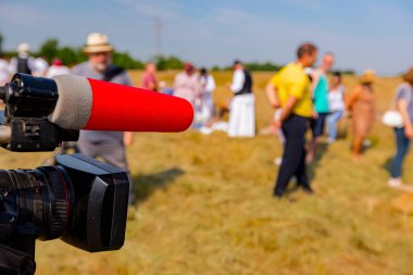 Mikrofonlu video kamera, çiftçiler kırsal alanda tahıl toplamaya başlamadan önce insanları eğlenmek için tripodun üzerinde duruyor..
