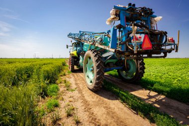 Traktörün düşük açılı görüntüsü geniş tarımsal püskürtücüleri sürüklerken, kırsal kırsal yolda giderken, tarım arazileri arasında zemin yolunda giderken.