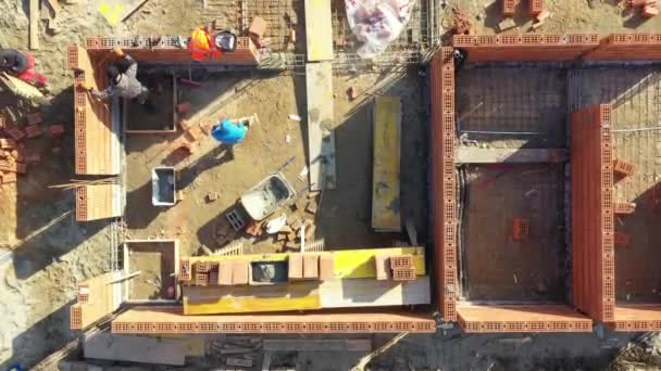 在建筑工地的高层视图之上 砖匠工人们正在用红色的砖块和砂浆筑起一堵新家的墙 大楼正在建造中 — 图库视频影像