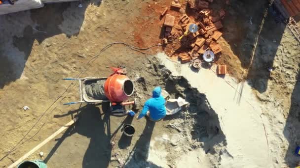 建物の場所区域の上の眺めの上に 建設労働者はコンクリート モルタルを作るようにミキサーを満たすためにシャベルを使用しています — ストック動画