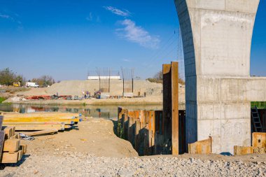 Temelde metal yığınlarıyla çevrili büyük gri beton sütun. Kalaslar, kirişler yere yerleştirilmiş, köprü kalıpları için ahşap profiller, nehir boyunca güçlendirilmiş direkler var..