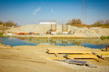 Açık havada depolama yapmak, kalaslar, kirişler yere yığılmış, ahşap profiller bir köprü kalıbı oluşturma ihtiyacı için, nehir boyunca inşaat halindeki köprü direkleridir..