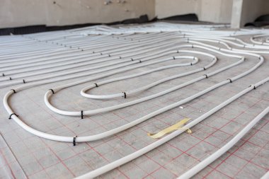 Yeni pirinç dağıtım sisteminin karmaşık eğrisinde bükülmüş ince beyaz boruların düşük açılı görüntüsü, inşaat halindeki bir konut binasında merkezi ısıtma katı için monte edilmiştir..