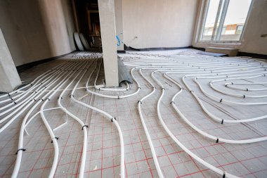 Yeni pirinç dağıtım sisteminin karmaşık eğrisinde bükülmüş ince beyaz boruların düşük açılı görüntüsü, inşaat halindeki bir konut binasında merkezi ısıtma katı için monte edilmiştir..