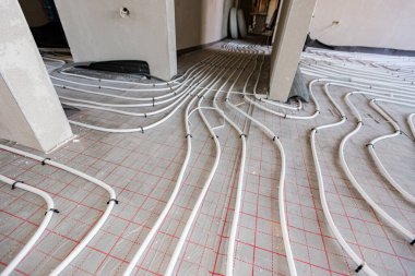 Yeni pirinç dağıtım sisteminin karmaşık eğrisinde bükülmüş ince beyaz boruların düşük açılı görüntüsü, inşaat halindeki bir konut binasında merkezi ısıtma katı için monte edilmiştir..