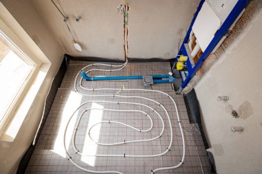 İnce beyaz borular yeni pirincin karmaşık eğrisiyle bükülmüş. Dağıtım sistemi manifoldu, bitmemiş banyoda merkezi ısıtma katı için monte edilmiş. İnşaat halindeki konut binası..