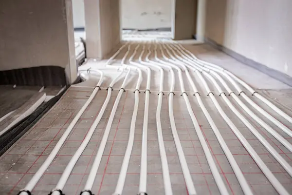 stock image Low angle view on thin white tubes bended in complex curve of new brass distribution system manifold mounted for central heating floor in a residential building under construction.