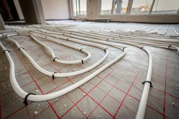 stock image Low angle view on thin white tubes bended in complex curve of new brass distribution system manifold mounted for central heating floor in a residential building under construction.