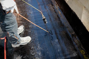 İşçi, propan pürmüz kullanılarak beton üzerine ziftle su yalıtımı kurulumunu ısıtıyor, eritiyor ve çalışma araçlarıyla yayılıyor. İnşaat halindeki konut binası su yalıtımı