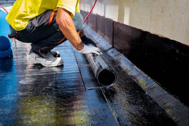 Worker in gloves prepare for melting, manually place and unroll rolled up, sheet of waterproofing installation over concrete. Residential building under construction placing water insulation clipart