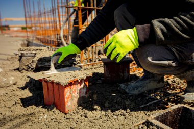 İşçi küp kalıbını betonla doldurmak için mala kullanıyor, gerilme ya da esneklik testi için örnek alıyor ve çimento karışımı döküm yapım temellerinin sıkıştırıcı güç testi yapıyor. Üst yüzeyi bitirmek için mala kullan.