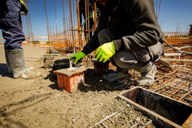 İşçi küp kalıbını betonla doldurmak için mala kullanıyor, gerilme ya da esneklik testi için örnek alıyor ve çimento karışımı döküm yapım temellerinin sıkıştırıcı güç testi yapıyor. Üst yüzeyi bitirmek için mala kullan.