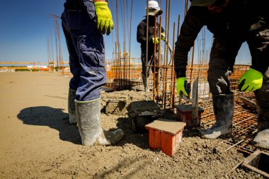 İşçi küp kalıbını betonla doldurmak için mala kullanıyor, gerilme ya da esneklik testi için örnek alıyor ve çimento karışımı döküm yapım temellerinin sıkıştırıcı güç testi yapıyor. Üst yüzeyi bitirmek için mala kullan.