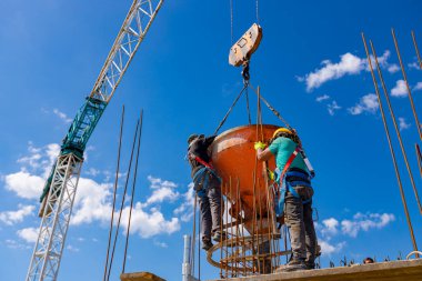 İnşaat işçileri konik metal kovaları boşaltıyorlar, taşınıyor ve beton karışımını yüksek tutuyorlar, binanın sütunları için dikey kalıba beton döküyorlar, koni tankını taşırken vinç kullanıyorlar..