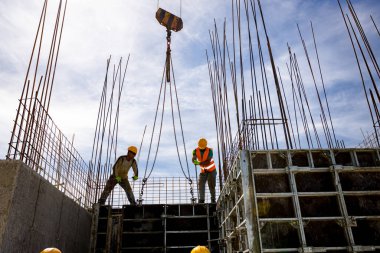 Kule vinci, çelik yelek ve miğferli inşaat işçilerinin güçlendirilmiş beton sütun için uzun tahta sökülebilir büyük küf yapmalarına yardımcı olur..