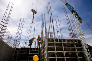 Kule vinci, çelik yelek ve miğferli inşaat işçilerinin güçlendirilmiş beton sütun için uzun tahta sökülebilir büyük küf yapmalarına yardımcı olur..
