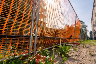 İstikrar için plastik çit ayağı geçici metal tel paneller, turuncu, plastik, güvenlik ağı ile sınırlı alan inşaat halindeki yeni tamamlanmamış çok katlı binanın etrafına yerleştirilmiş..