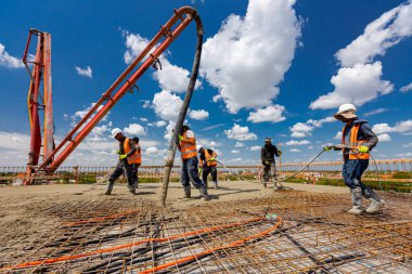 Lastik çizmeli inşaat işçisi pompa tüpünü doğru yöne yönlendiriyor, beton tabakası döküyor, betonu kare takviyesinin üzerine döküyor. Sıvı betonu sıkıştırmak için elektrikli alet, sıkıştırıcı kullanıyorlar.,
