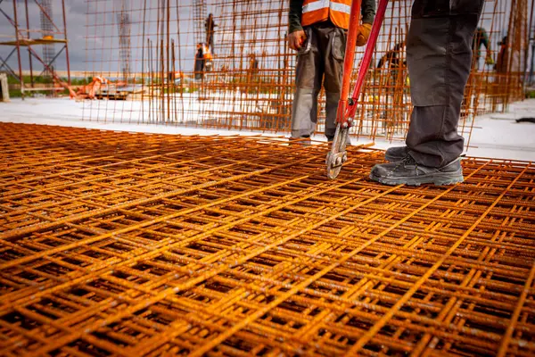 stock image Worker is standing on pile of rusty rectangle steel, reinforcement for concrete as cutting reinforcement grid, mesh with bolt cutters at building site.