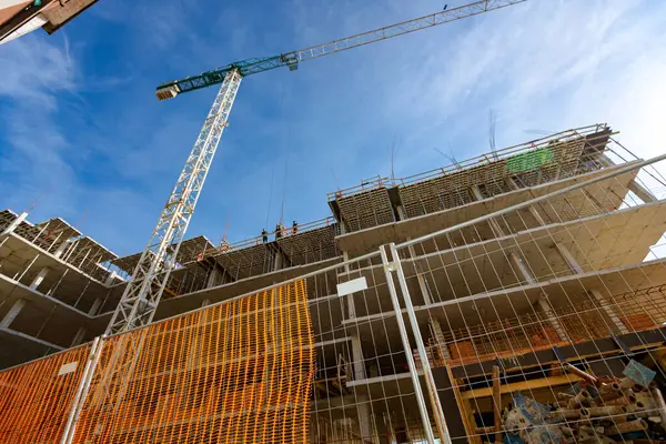 stock image Confined space with orange, plastic, safety mesh is placed around unfinished multi-storey building with tower crane, residential complex under construction.