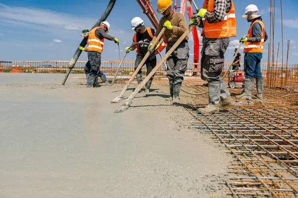 stock image Team of construction workers are pouring and leveling fresh concrete using handmade tool over rectangular armature.