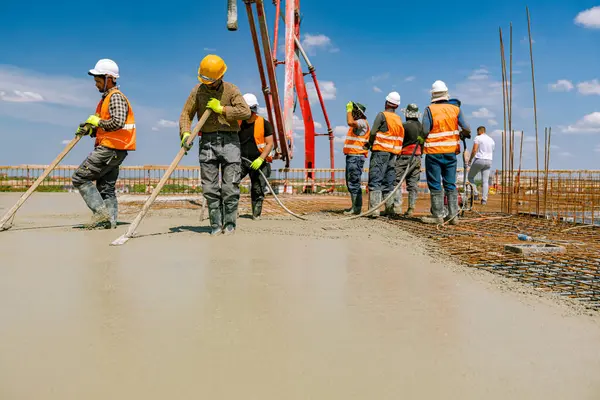 stock image Team of construction workers are pouring and leveling fresh concrete using handmade tool over rectangular armature.