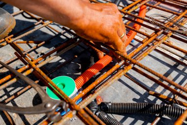 Korunaklı plastik hortumlar kurarken, kablolar için, dağıtım kutusuna yerleştirmek ve bağlamak için paslı demirin altında, üzerlerine beton dökmek için hazırlanan işçilerin elleri. 