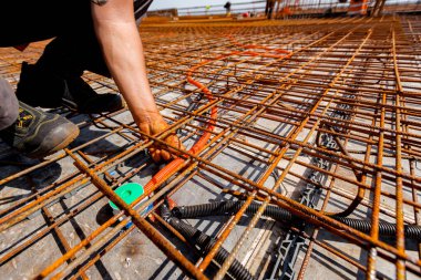 Korunaklı plastik hortumlar kurarken, kablolar için, dağıtım kutusuna yerleştirmek ve bağlamak için paslı demirin altında, üzerlerine beton dökmek için hazırlanan işçilerin elleri. 