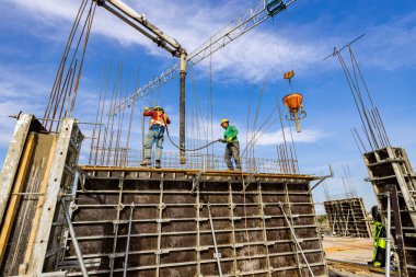 İnşaat işçisi çeliği güçlendiren sütunlar inşa etmek için kalıp içine beton dökmek için pompa tüpü kullanıyor. Mason taze sıvı betonu sıkıştırmak için elektrikli alet, sıkıştırıcı ve vibratör kullanıyor..