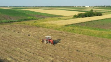 Tırmıkla bağlı traktör dönüyor ve kuru otları topluyor saman demetleri ya da balyalar için uzun kuyruklar oluşturuyor. Tarım makineleri, çayırda kurumuş mahsulü döndürmek için parmak tırmığı.