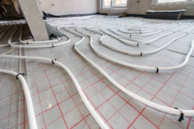 Yeni pirinç dağıtım sisteminin karmaşık eğrisinde bükülmüş ince beyaz boruların düşük açılı görüntüsü, inşaat halindeki bir konut binasında merkezi ısıtma katı için monte edilmiştir..