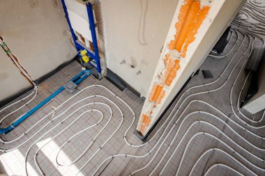 İnce beyaz borular yeni pirincin karmaşık eğrisiyle bükülmüş. Dağıtım sistemi manifoldu, bitmemiş banyoda merkezi ısıtma katı için monte edilmiş. İnşaat halindeki konut binası..