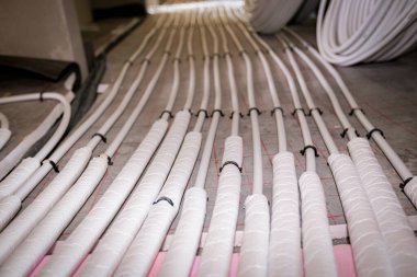 Yeni pirinç dağıtım sisteminin karmaşık eğrisinde bükülmüş ince beyaz boruların düşük açılı görüntüsü, inşaat halindeki bir konut binasında merkezi ısıtma katı için monte edilmiştir..