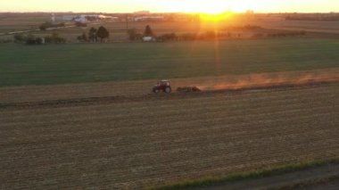 Dolly 'nin traktörü çekiş makinesi olarak kullanması, disk kirişi kırıcı, toprağı bir sonraki hasat için hazırlıyor. Kuş sürüsü yiyecek aramak için tarımsal makineyi takip ediyor. Gün batımı ve arka plan