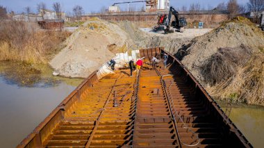 İşçiler eski büyük bir gemiyi keserken, mavnayı parçalara ayırırken, paslı metali kırbaç için keserken, asetilen meşalesi, geri dönüşüm, kıvılcımlar uçuşurken, üst görünümde işçiler görülüyor..
