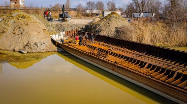 İşçiler eski büyük bir gemiyi keserken, mavnayı parçalara ayırırken, paslı metali kırbaç için keserken, asetilen meşalesi, geri dönüşüm, kıvılcımlar uçuşurken, üst görünümde işçiler görülüyor..