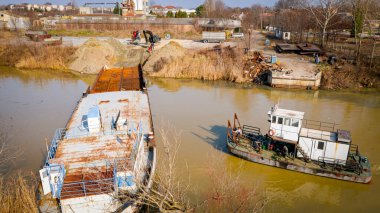 Kazıcının, çekicinin ve römorkörün üzerinde, eski yük gemisinin yatağının bir kısmını çekerken, mavna, nehir kıyısında, kazma, sökme gemisi, kırbaç için metal, geri dönüşüm,.